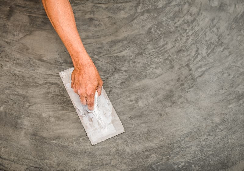 A hand with a trowel on a concrete floor